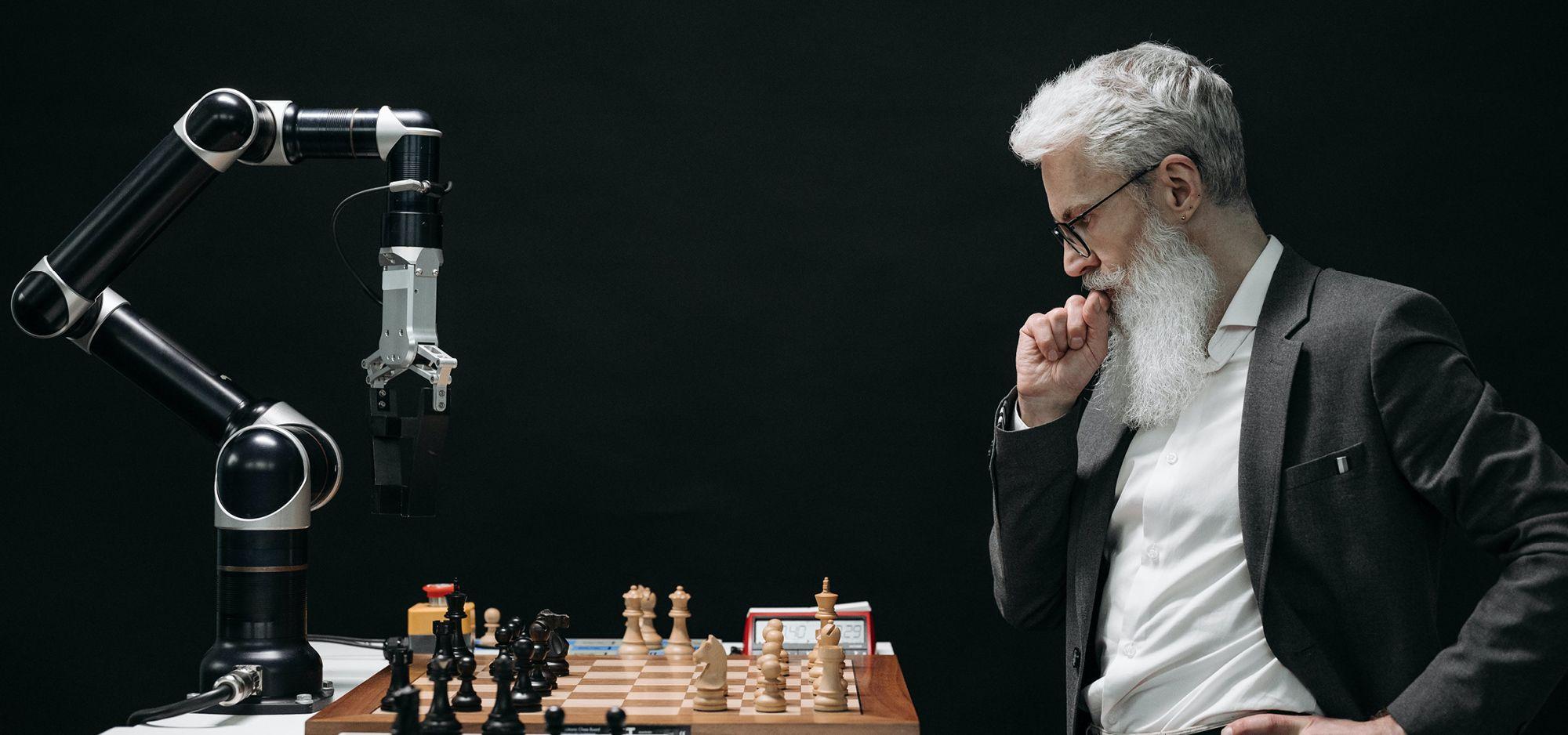 A man with a beard playing chess with at a robot to thoroughly test his skills.